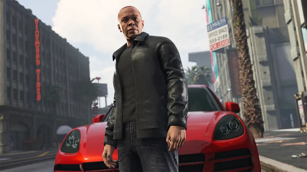 this is a gta online screenshot of dr. dre is stood in front of a red car on vinewood boulevard. you can see the vinewood walk of fame to the right on the floor, palm trees and the theatre buildings behind him